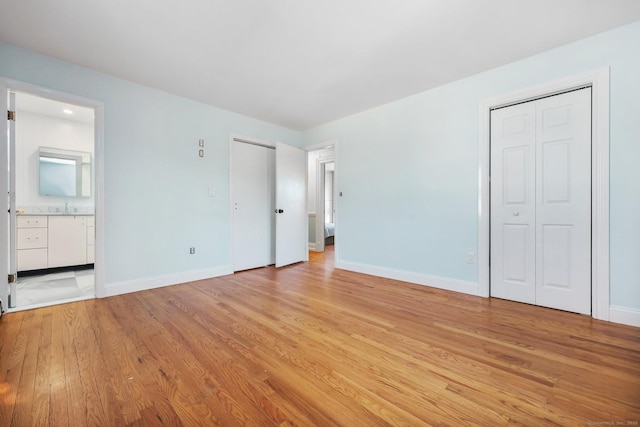 unfurnished bedroom with ensuite bathroom, light wood-type flooring, two closets, and baseboards