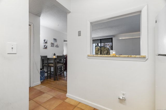 hallway featuring baseboards, a textured ceiling, and tile patterned floors