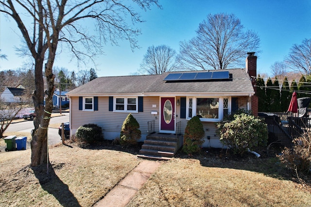 view of front of home featuring a shingled roof, a chimney, and solar panels