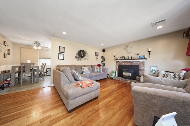 living area featuring light wood finished floors, recessed lighting, visible vents, a ceiling fan, and a brick fireplace