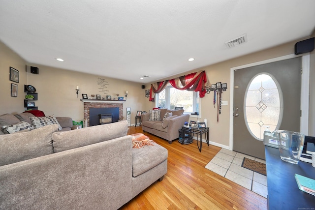 living area with recessed lighting, visible vents, baseboards, a brick fireplace, and light wood finished floors