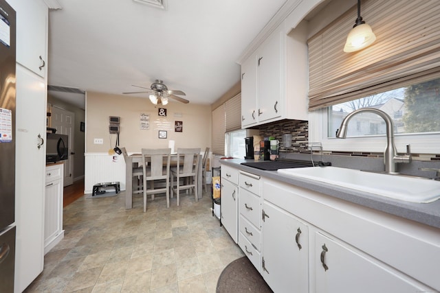 kitchen with a sink, a ceiling fan, white cabinets, wainscoting, and backsplash