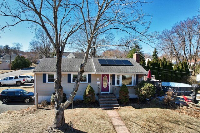 ranch-style house featuring roof with shingles, a chimney, and roof mounted solar panels