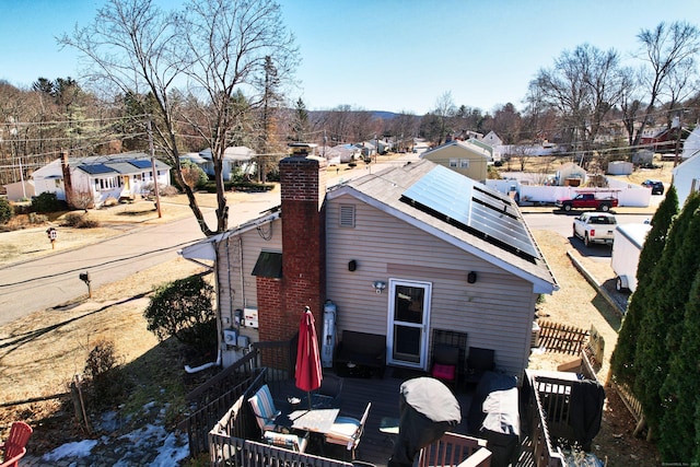 rear view of house with roof mounted solar panels, a chimney, fence, and a residential view