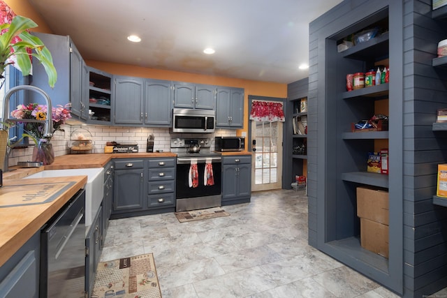 kitchen with stainless steel appliances, gray cabinets, open shelves, and wooden counters