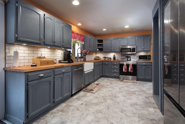 kitchen with tasteful backsplash, butcher block countertops, stainless steel appliances, a sink, and recessed lighting