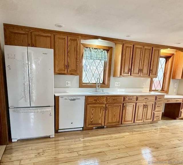 kitchen featuring white appliances, light wood-style flooring, brown cabinets, and a sink