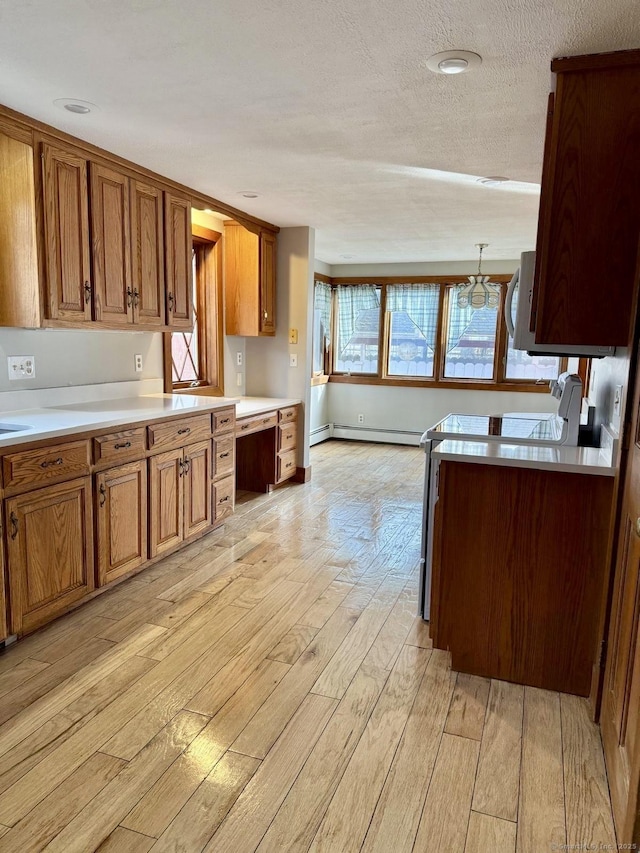 kitchen featuring brown cabinetry, built in study area, light wood-style flooring, light countertops, and a baseboard heating unit