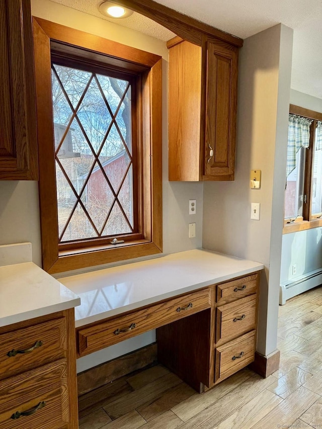 kitchen with a baseboard heating unit, light wood-type flooring, brown cabinetry, and light countertops