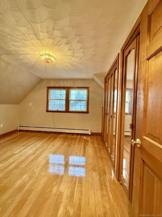 bonus room featuring a baseboard heating unit, vaulted ceiling, and light wood-style floors