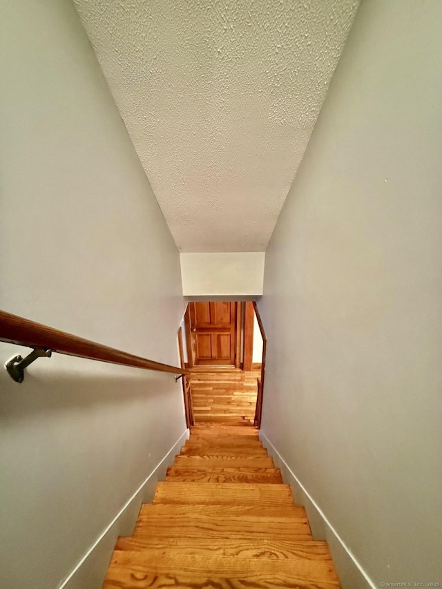 stairway with a textured ceiling, wood finished floors, and baseboards