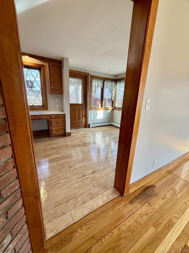 kitchen with a baseboard radiator, a healthy amount of sunlight, built in study area, and light wood-style flooring