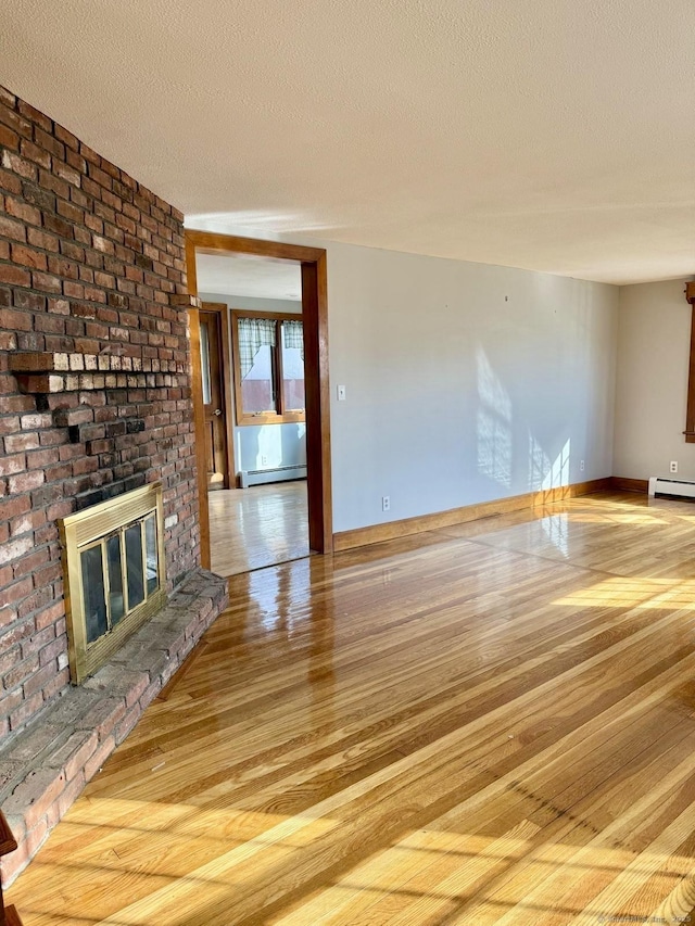 unfurnished living room featuring a brick fireplace, baseboard heating, light wood finished floors, and a textured ceiling