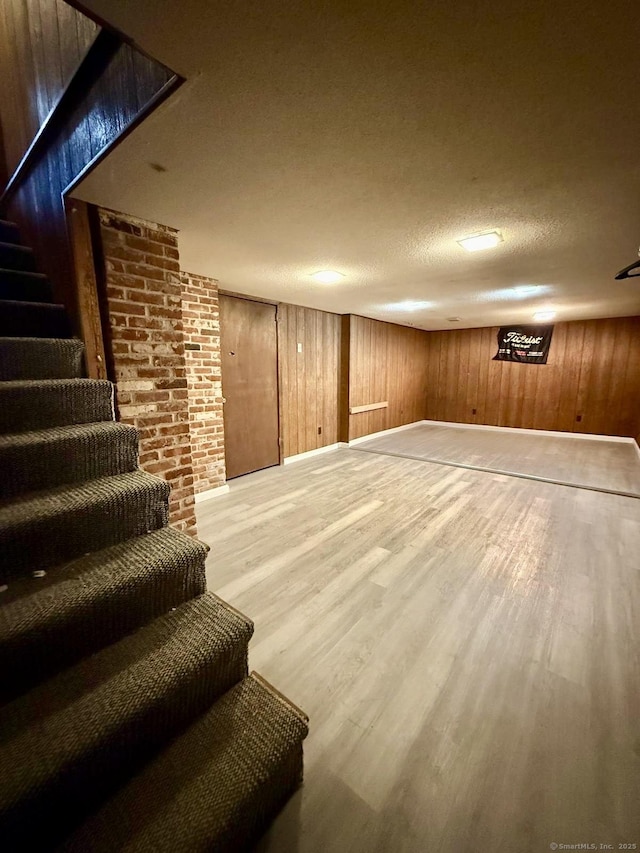 finished basement featuring baseboards, stairway, wood finished floors, a textured ceiling, and wood walls