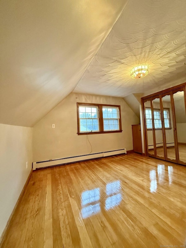 additional living space featuring a baseboard radiator, vaulted ceiling, baseboards, and wood-type flooring