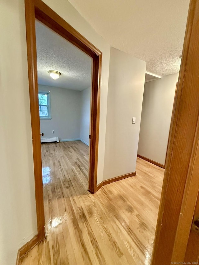 corridor featuring light wood-type flooring, a textured ceiling, baseboards, and a baseboard radiator