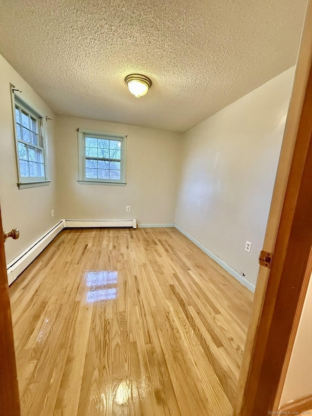 empty room featuring light wood finished floors, a baseboard radiator, and baseboards