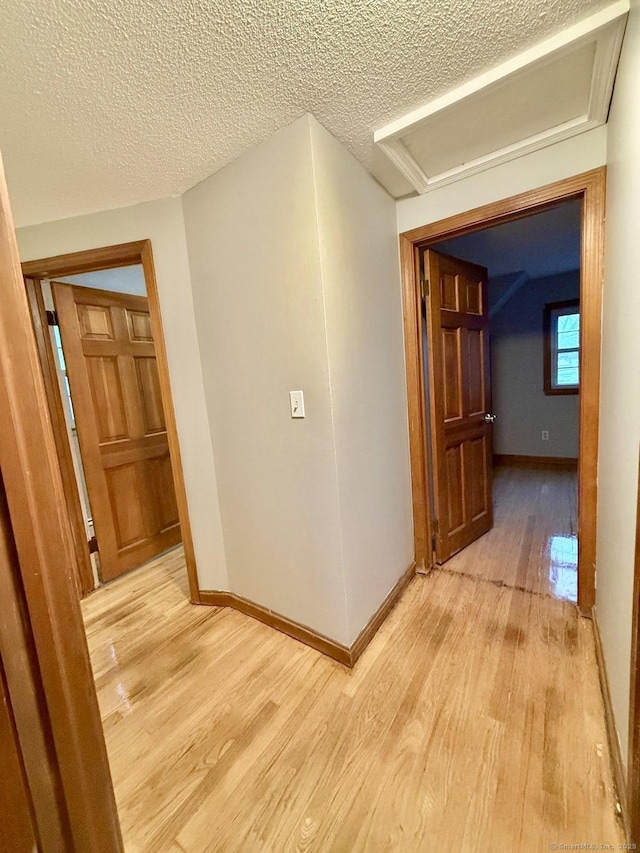 hall with light wood-type flooring, a textured ceiling, and baseboards