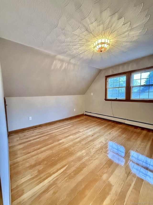 additional living space featuring light wood-type flooring, baseboards, vaulted ceiling, and baseboard heating