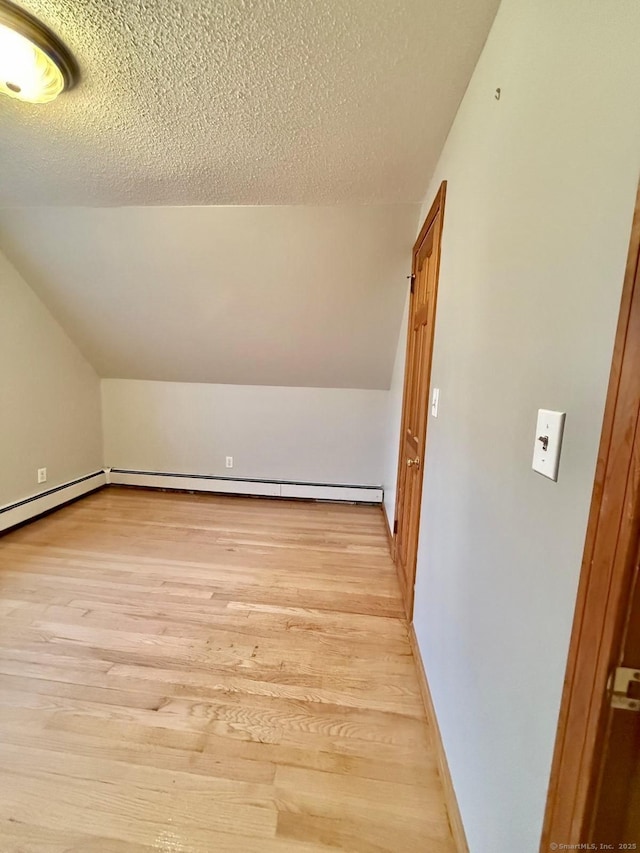 additional living space with baseboards, vaulted ceiling, light wood-style flooring, and a textured ceiling