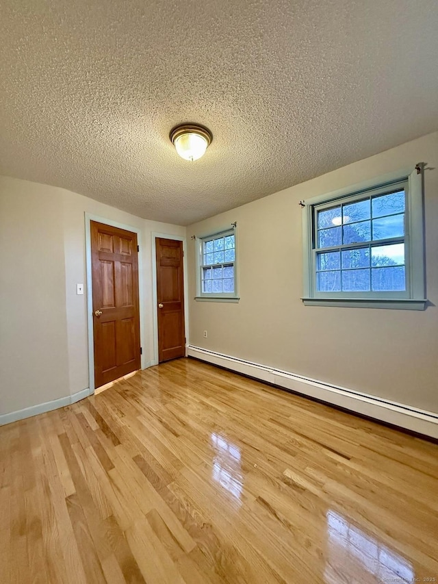 unfurnished bedroom featuring light wood-style floors, baseboards, a textured ceiling, and baseboard heating