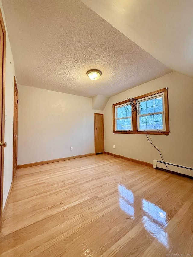 spare room with vaulted ceiling, a textured ceiling, and light wood-type flooring