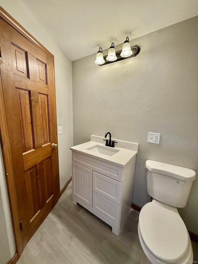 bathroom with toilet, baseboards, wood finished floors, and vanity