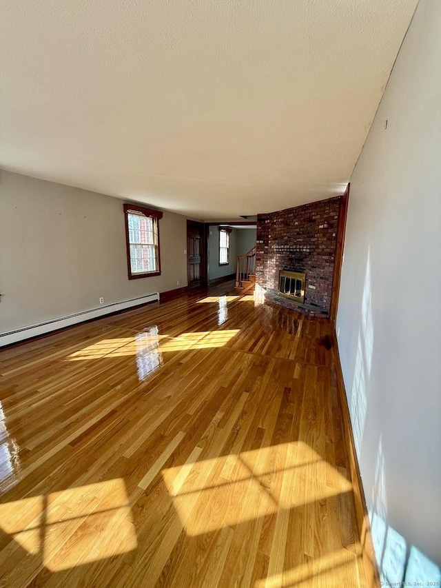 unfurnished living room with baseboard heating, a fireplace, wood finished floors, and baseboards