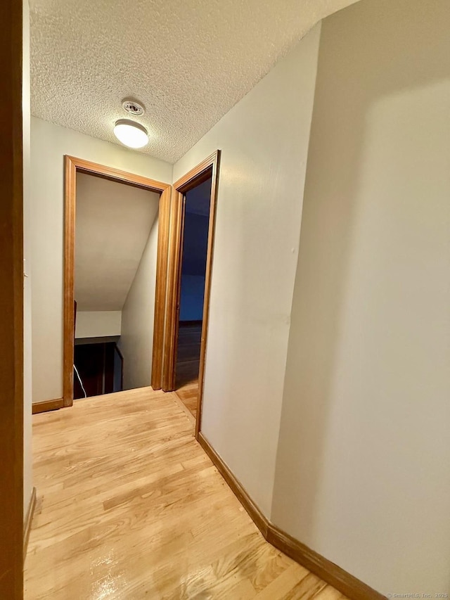 hallway featuring a textured ceiling, light wood-type flooring, and baseboards