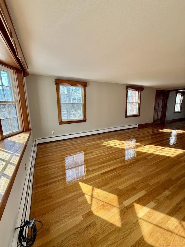 unfurnished living room featuring a baseboard heating unit, wood finished floors, and baseboards