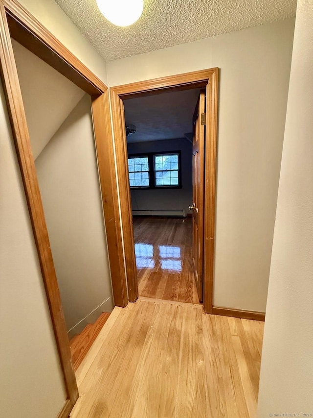 hallway featuring a baseboard heating unit, a textured ceiling, baseboards, and wood finished floors