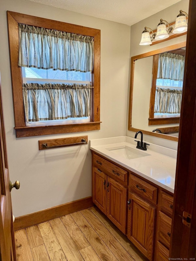 bathroom with baseboards, vanity, a textured ceiling, and wood finished floors