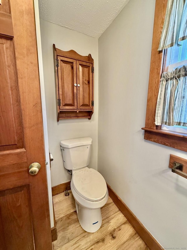 bathroom with a textured ceiling, wood finished floors, toilet, and baseboards