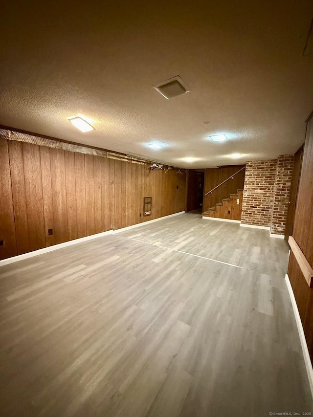 finished basement with wooden walls, a textured ceiling, and wood finished floors