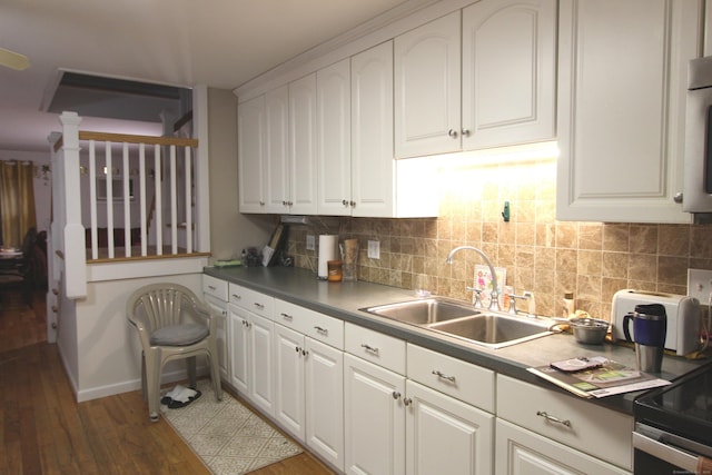 kitchen featuring tasteful backsplash, white cabinets, dark countertops, dark wood-style flooring, and a sink