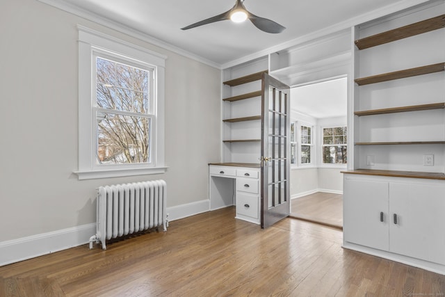 interior space with baseboards, light wood-style floors, built in study area, radiator heating unit, and crown molding