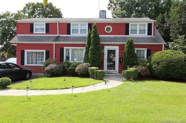 view of front facade featuring a shingled roof, a front yard, and a chimney