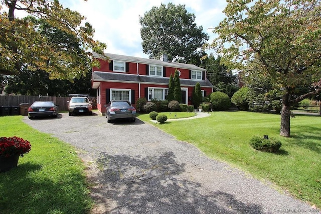 view of front of property featuring aphalt driveway, a front lawn, a chimney, and fence