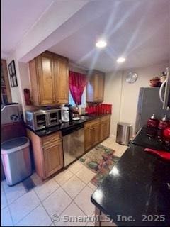 kitchen featuring light tile patterned floors, stainless steel appliances, dark countertops, brown cabinetry, and a sink