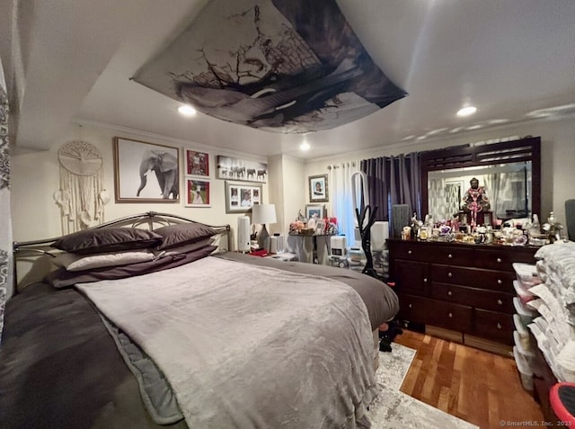 bedroom featuring a tray ceiling, ornamental molding, wood finished floors, and recessed lighting