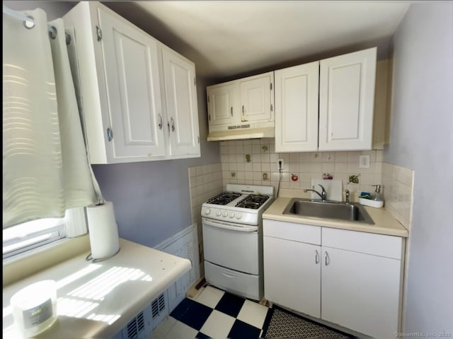 kitchen with under cabinet range hood, white range with gas stovetop, white cabinetry, and a sink