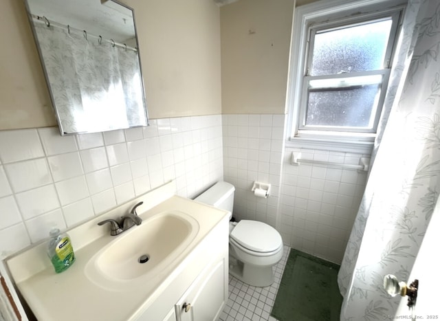 bathroom featuring wainscoting, toilet, tile patterned flooring, vanity, and tile walls