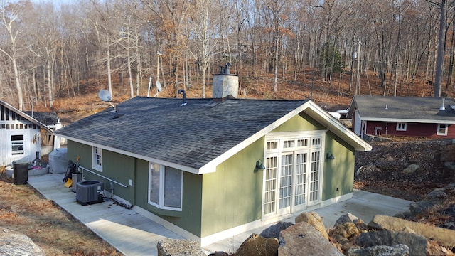 view of property exterior featuring central air condition unit, a shingled roof, and a chimney