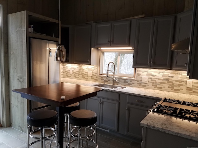 kitchen featuring under cabinet range hood, tasteful backsplash, light stone counters, and a sink