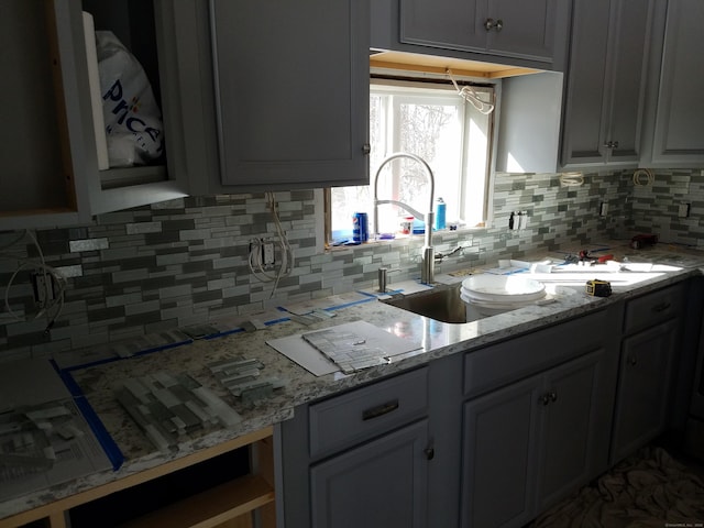 kitchen featuring a sink, light stone counters, and backsplash