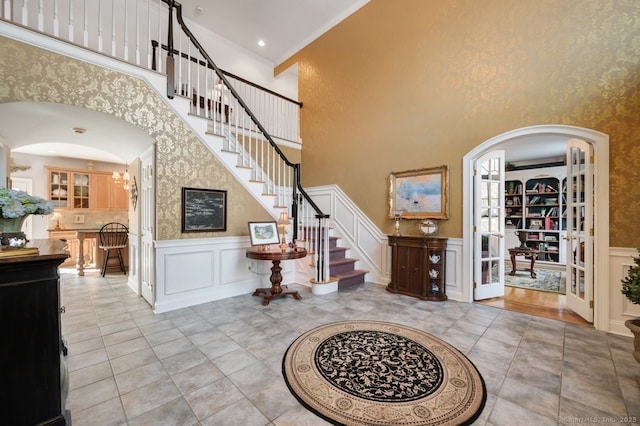 entrance foyer with arched walkways, a decorative wall, a wainscoted wall, stairway, and crown molding