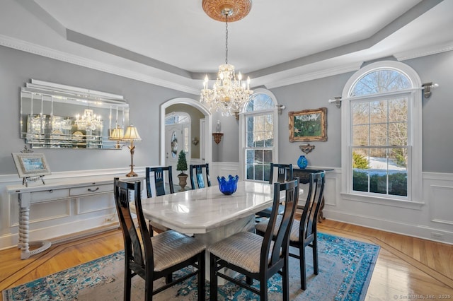 dining space featuring arched walkways, a wainscoted wall, light wood finished floors, a raised ceiling, and an inviting chandelier