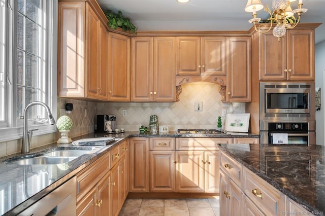 kitchen with light tile patterned floors, a sink, appliances with stainless steel finishes, decorative backsplash, and dark stone countertops