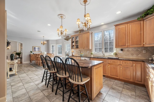 kitchen with a notable chandelier, a kitchen island, a kitchen breakfast bar, hanging light fixtures, and dark stone countertops