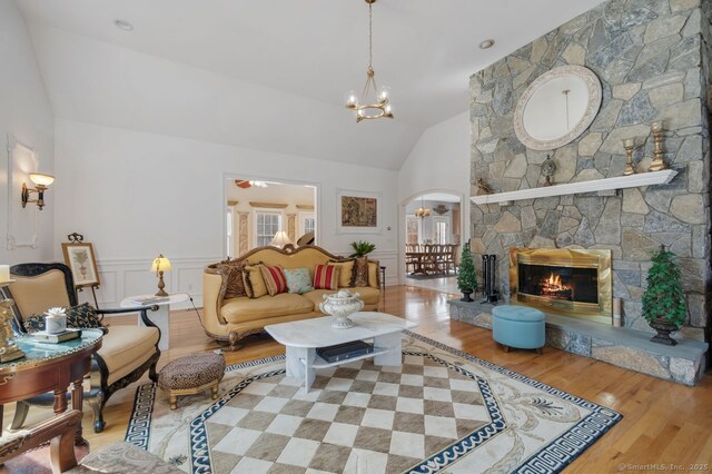 living area with arched walkways, a wainscoted wall, a fireplace, light wood-style floors, and vaulted ceiling